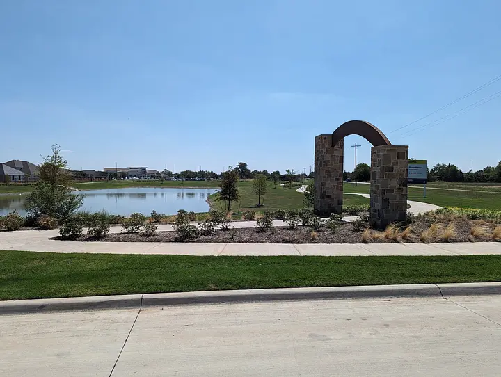 Stone archway by a pond with landscaped plants in the foreground, under a clear blue sky.