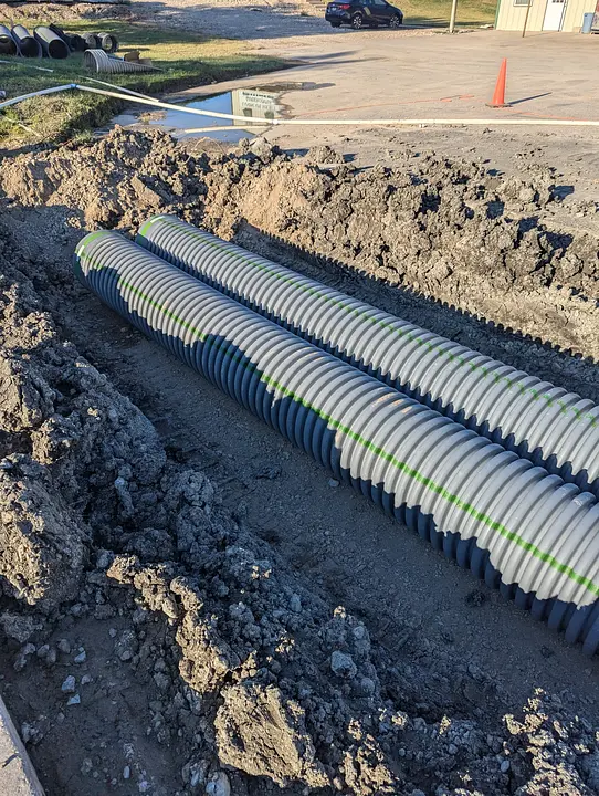Two large corrugated pipes in a trench at a construction site, with dirt piles on the sides.