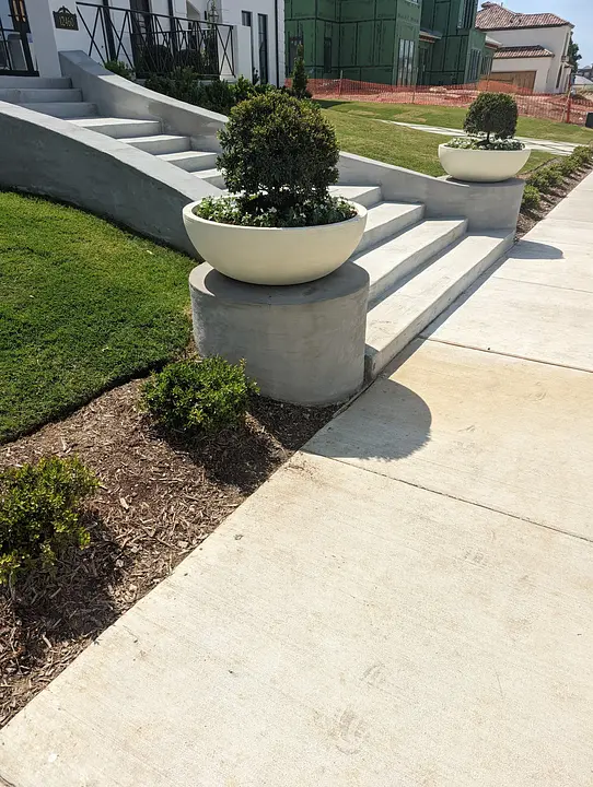 Concrete steps with round planters and greenery, leading to a building entrance.